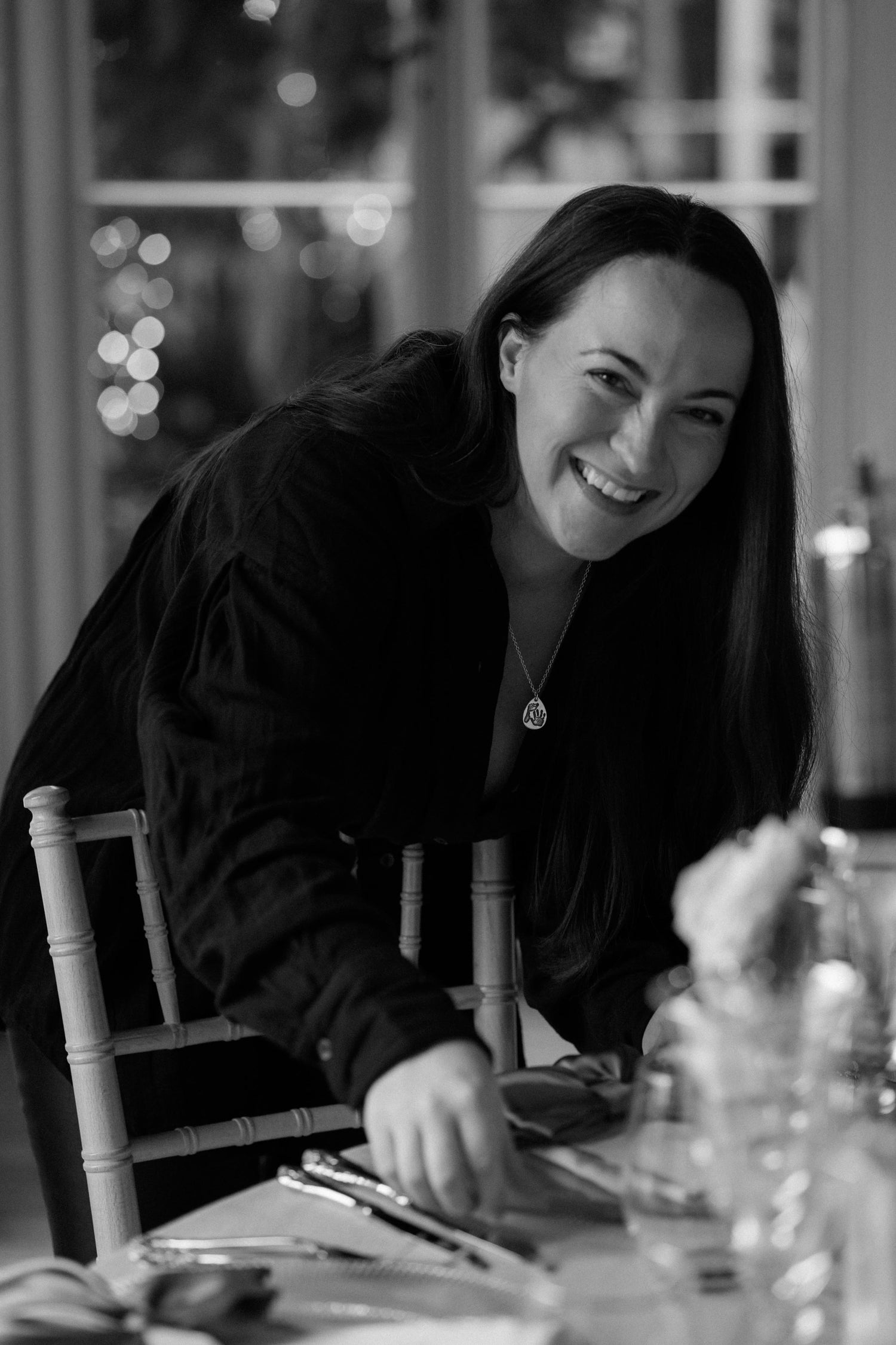 A black and white image of Gemma Anderson, creator of Atria UK, smiling to the camera while placing wedding menus on a table