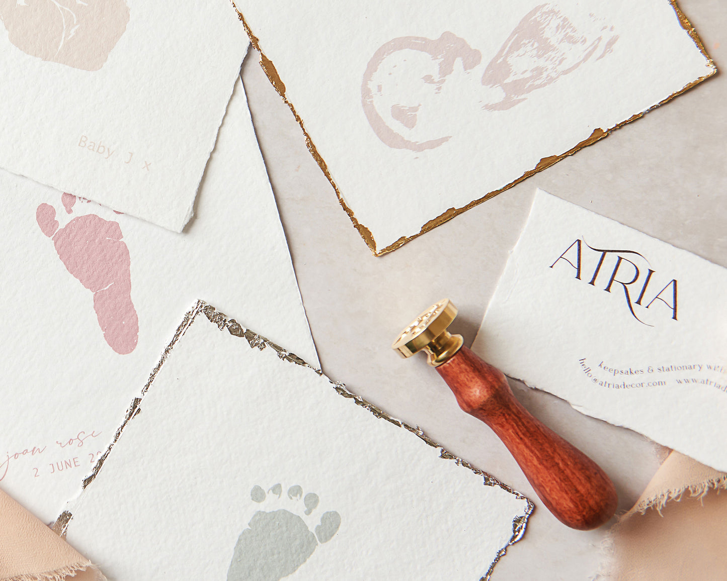 A close up image of various keepsakes from our collection, showing the different handmade paper edges. These include; natural deckle edges which are textured and feathery, a deckle edge with gold colour metal leaf applied and a deckle edge with a silver colour metal leaf applied. The metal leaf gilding shown is textural and has a raw edge to fit with the natural textures on the handmade paper it is applied to. It is applied to all for edges of the print creating a border around 2-4 millimetres  thick.