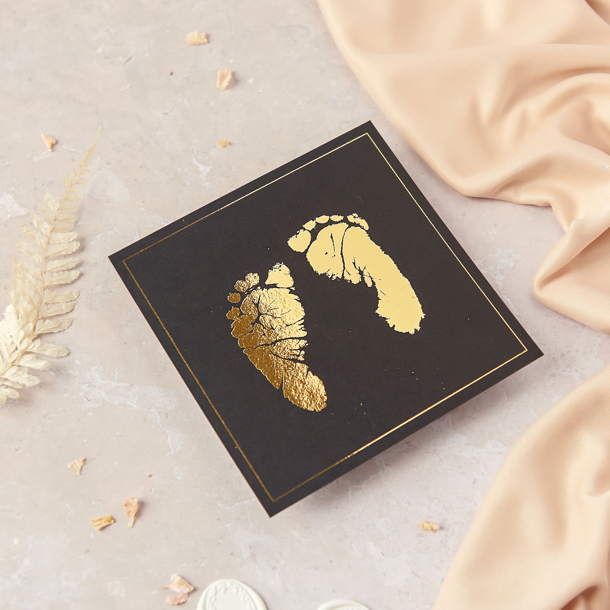 This photograph shows a pair of baby's feet, recreated using gold foil on to black cardstock. This foot print pair keepsake has been created on to 5 inch square card, although as standard pairs of prints are created on A5 size cardstock.