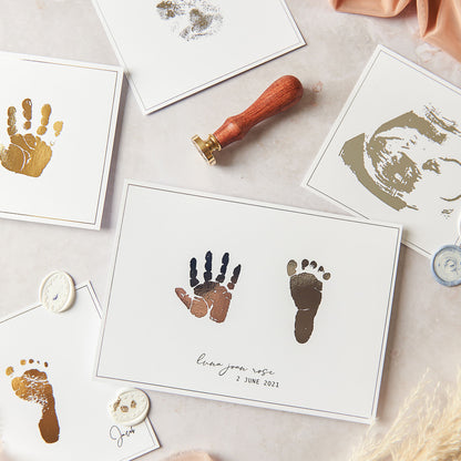 This photograph shows a collection of our foiled keepsake gifts including (clockwise from top): A Silver foil paw print on 5 inch white card, A silver foil baby scan on 5 inch white cardstock, An A5 hand and foot print pair in silver foil on white card, A gold foil baby foot print on 5 inch square white card and finally a hand print keepsake in gold foil on white card.